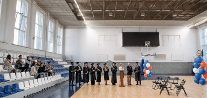 A graduation ceremony held in an indoor gymnasium with graduates and an audience.